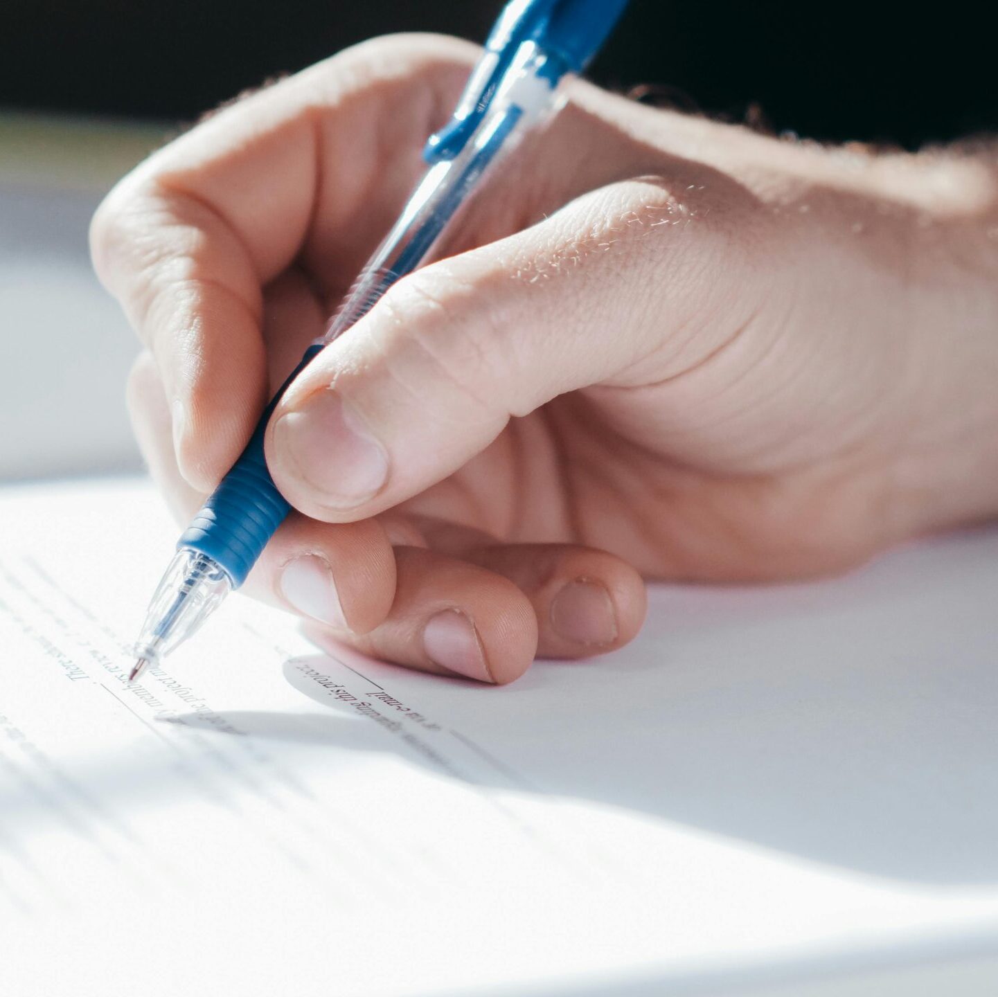A detailed shot of a hand writing with a blue pen on a piece of paper.