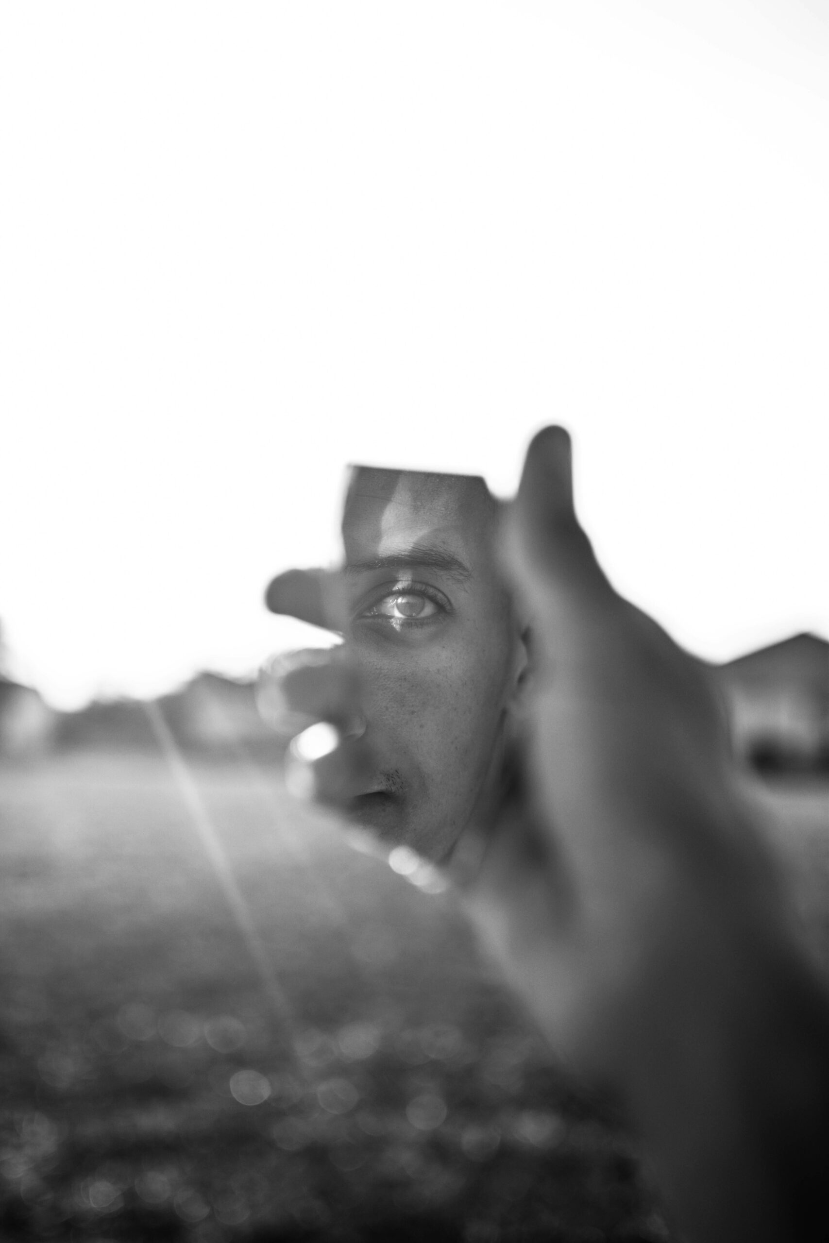 Creative black and white portrait featuring a man's reflection in a broken mirror piece, held by a hand.